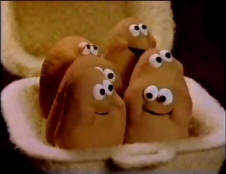 Image of a paper box container with six sentient McDonalds chicken nugget puppets, the creatures themselves made of unknown golden brown material. They all wear a gleeful and cheeky expression with wide, curious eyes. Possibly just born.